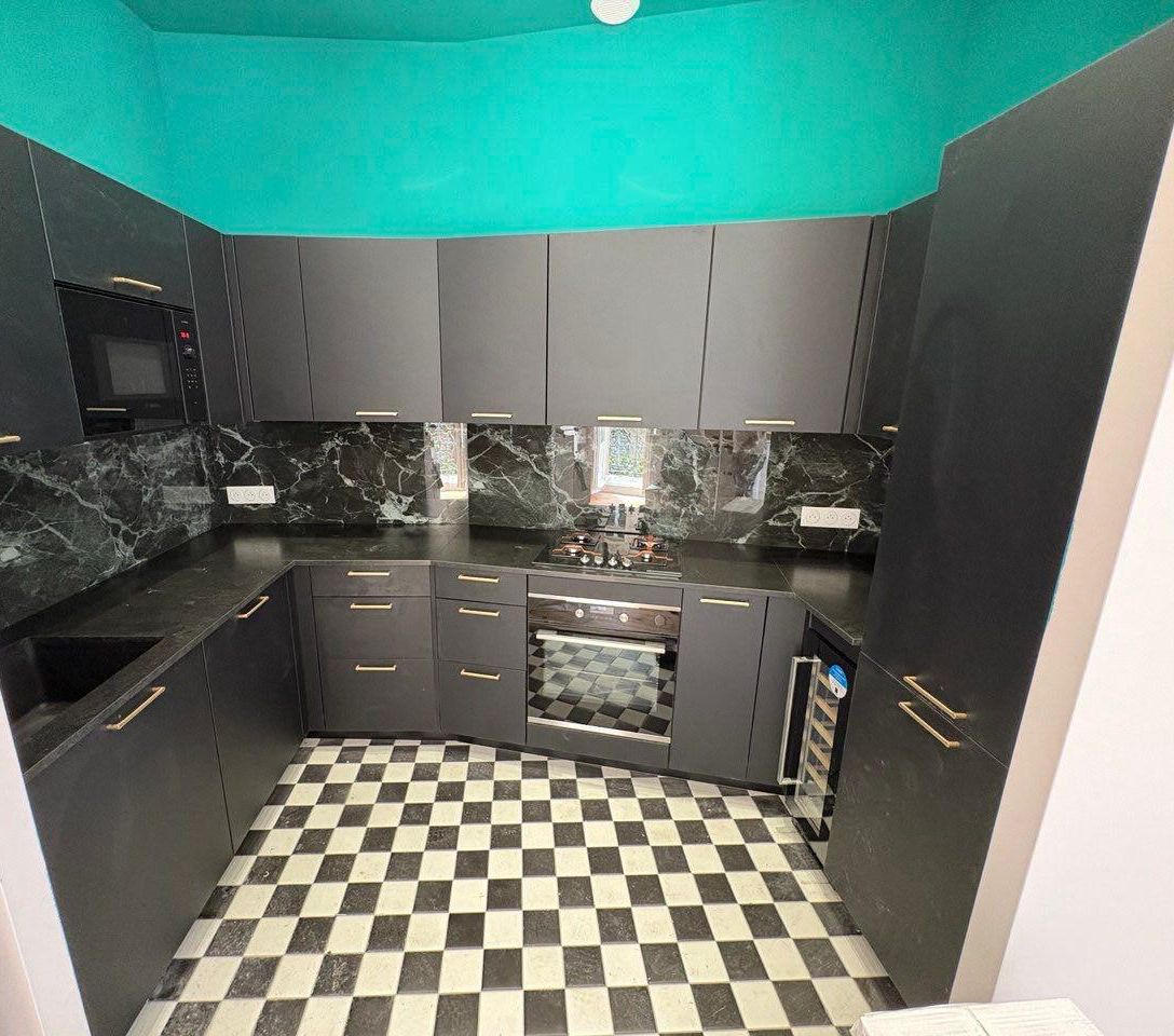 Cuisine aux meubles noirs mats, poignées dorées, crédence en marbre vert et sol en damier