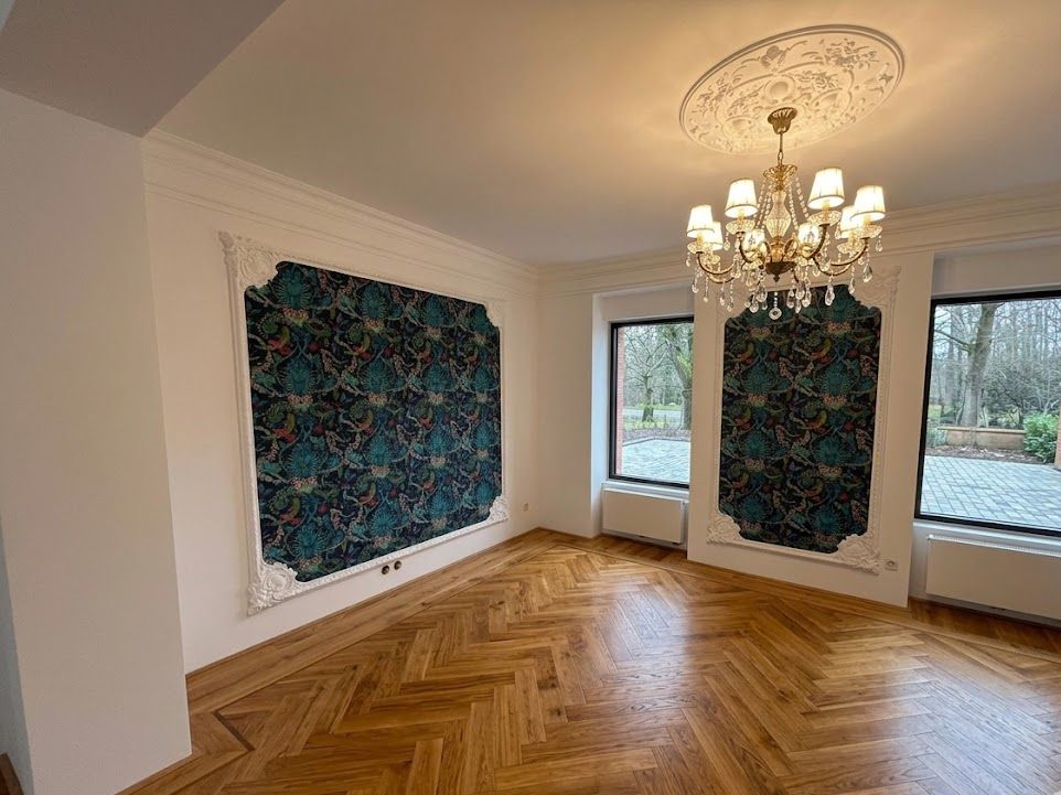 La même pièce terminée : papier peint encadré de moulures, lustre, parquet