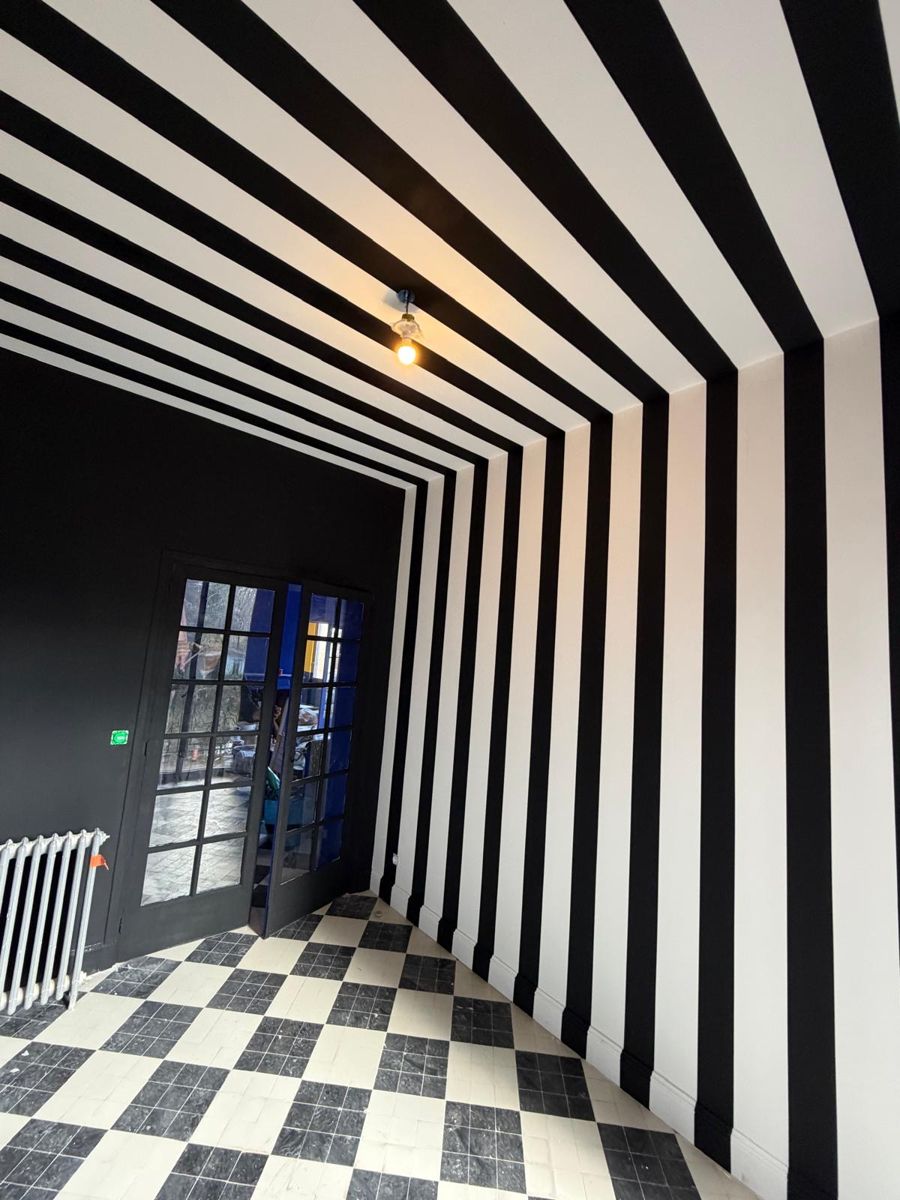 Pièce peinte en rayures noires et blanches du mur au plafond, sol en carreaux damier noir et blanc