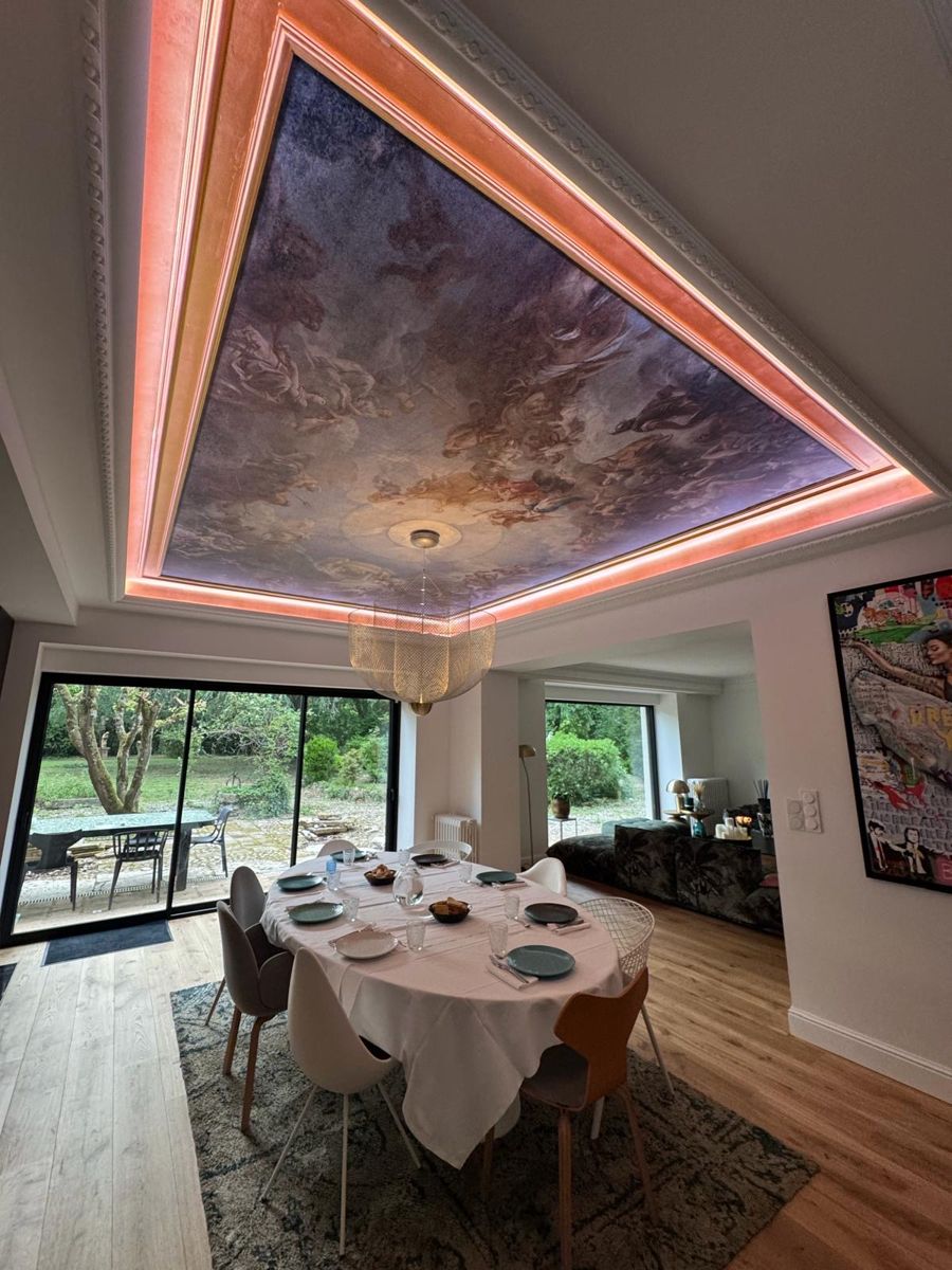 Plafond en caisson avec fresque peinte, éclairage indirect par ruban lumineux, suspension dorée au-dessus de la table